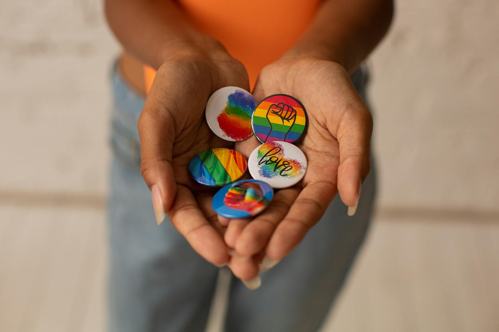 Hands holding colorful LGBT pride pins with rainbow designs.