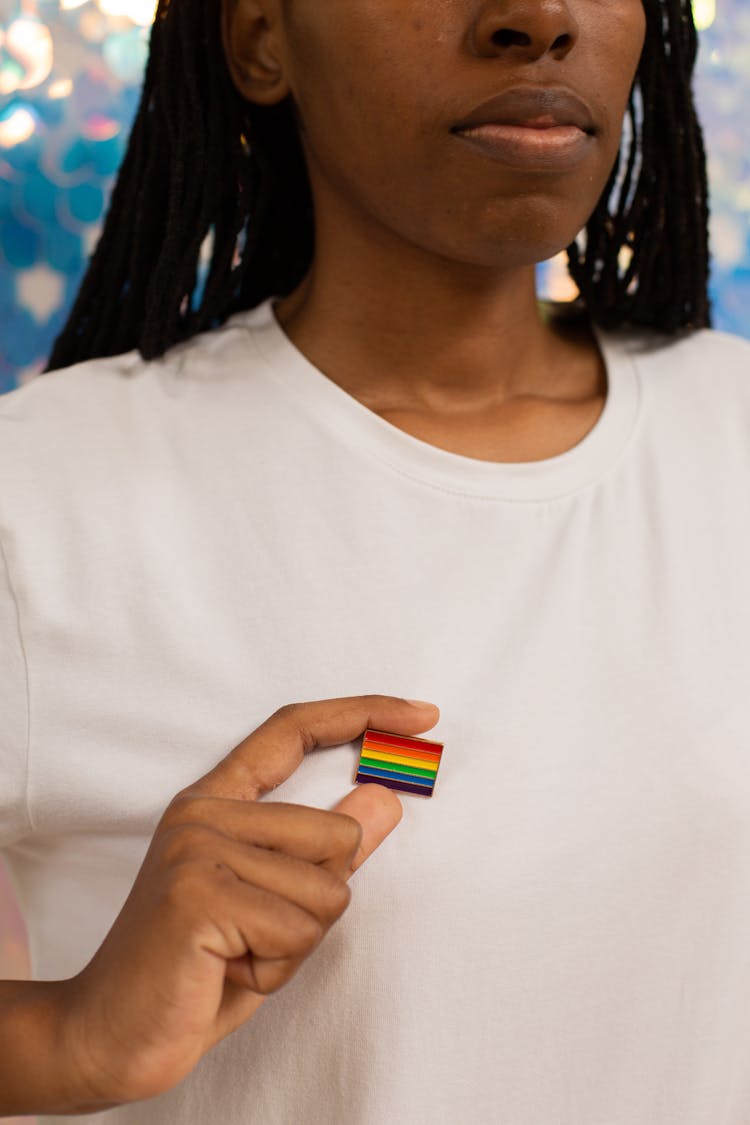 A Person In White Shirt Holding A Rainbow Pin On It's Shirt