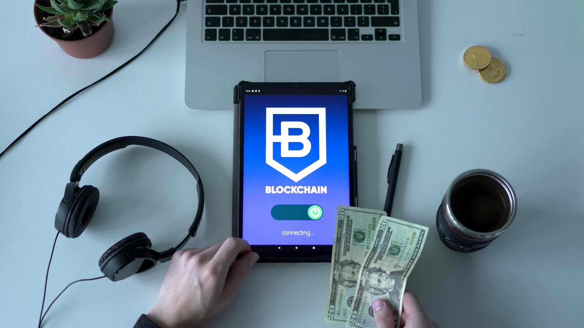 Overhead view of blockchain technology tablet with cash and modern workspace essentials.