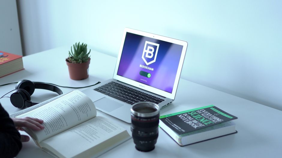 A laptop displaying blockchain technology in a modern workspace with books and headphones. A laptop displaying blockchain technology in a modern workspace with books and headphones.