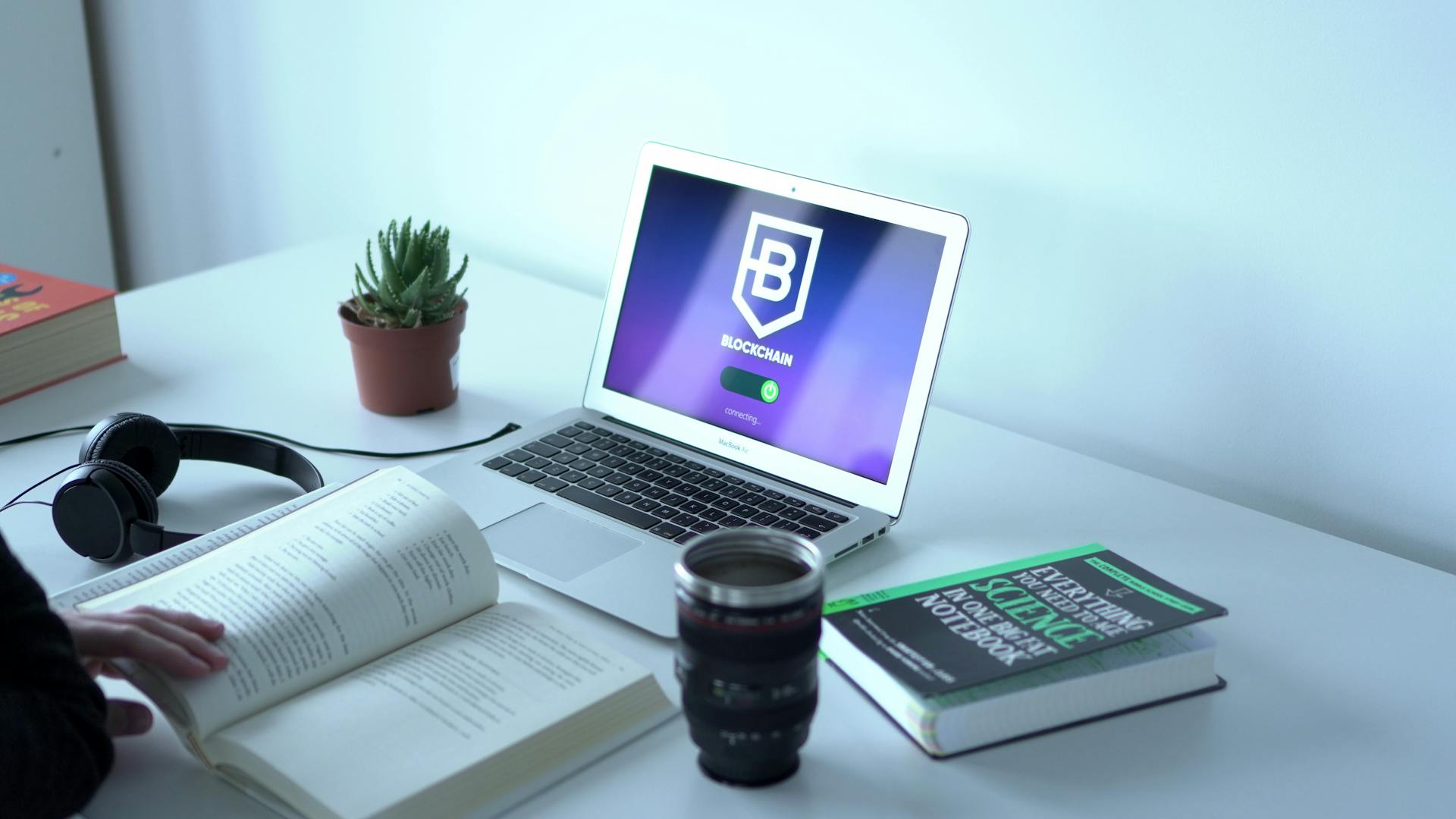 A laptop displaying blockchain technology in a modern workspace with books and headphones.