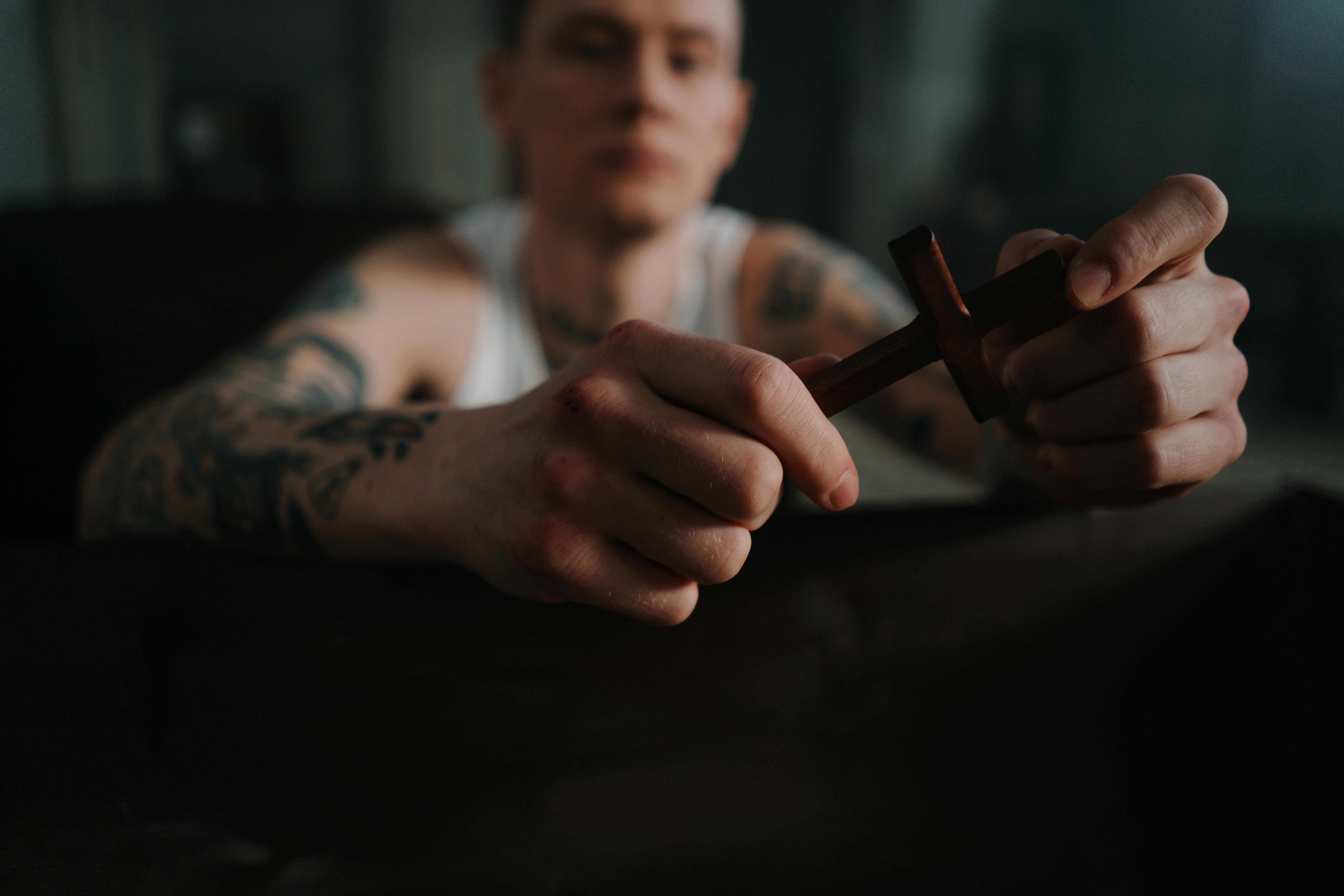 A tattooed man holding a wooden cross, symbolizing faith and contemplation indoors.