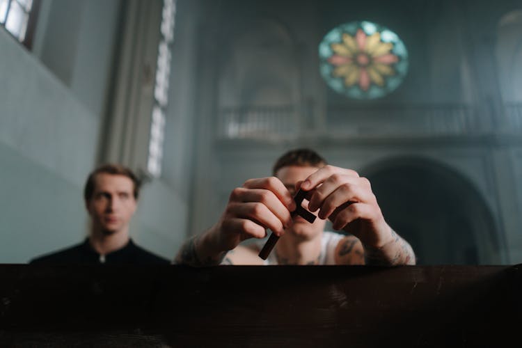 Tattooed Man Holding A Crucifix Sitting Beside A Priest