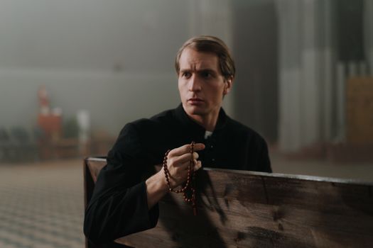 A Priest Holding a Rosary while Sitting on a Pew