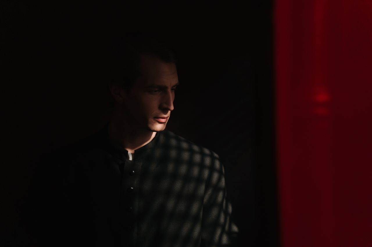 a priest stands solemnly in a dimly lit confessional casting dramatic