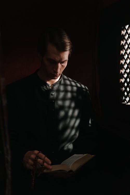 Free A Priest Reading a Bible in the Dark Stock Photo