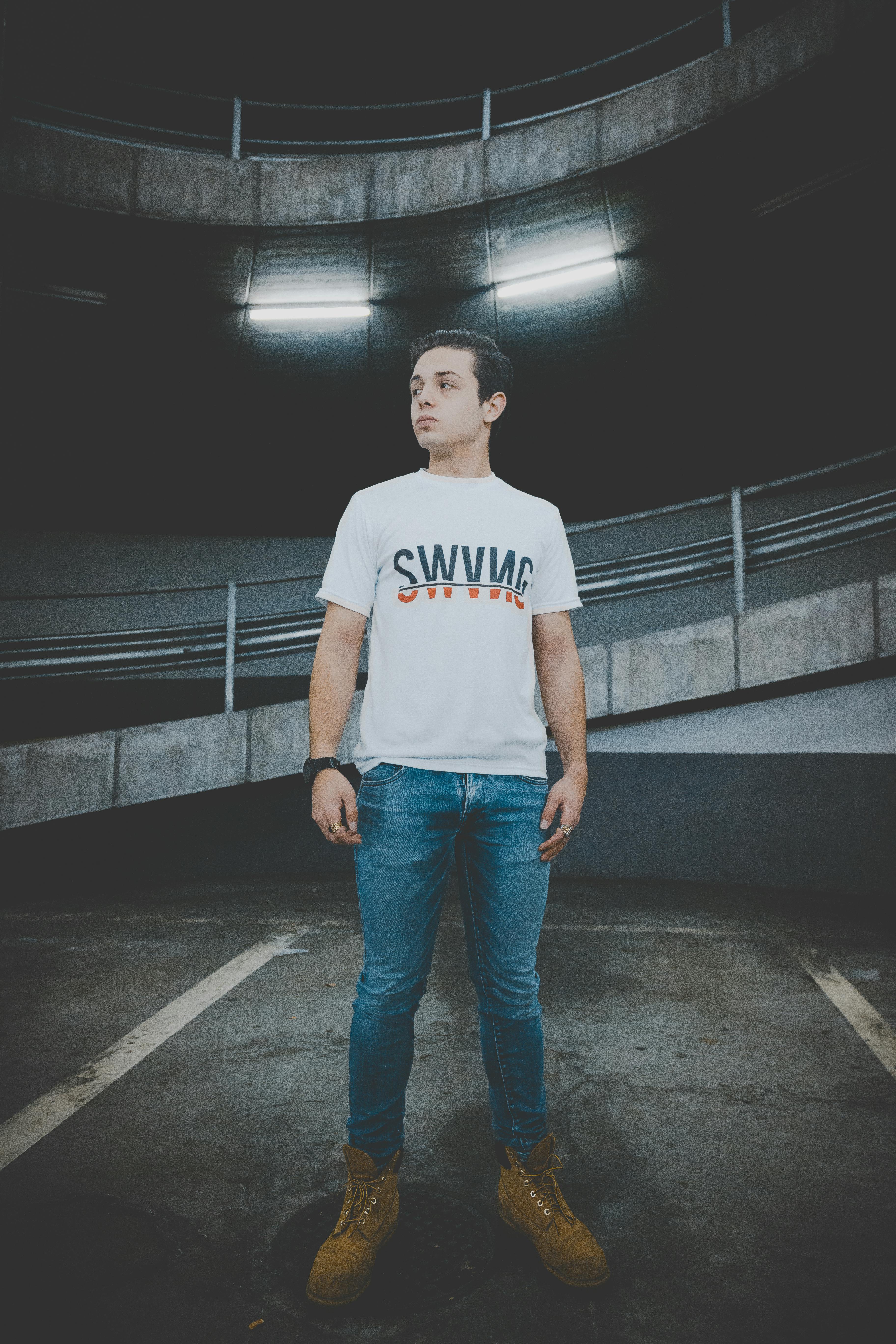 Download Man Wearing White T-shirt and Blue Jeans Standing on Black ...