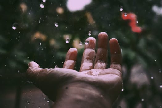 A hand reaching up to catch rain droplets, set against a blurred natural background.