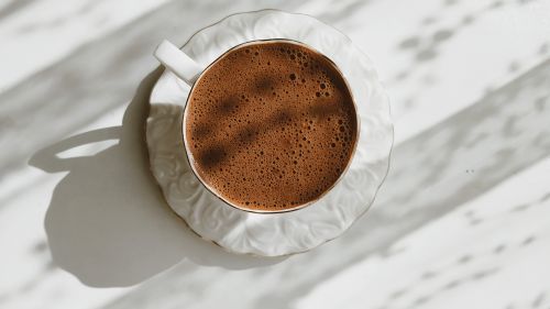 Free Aerial view of a foamy coffee in an ornate ceramic cup with sunlight. Stock Photo