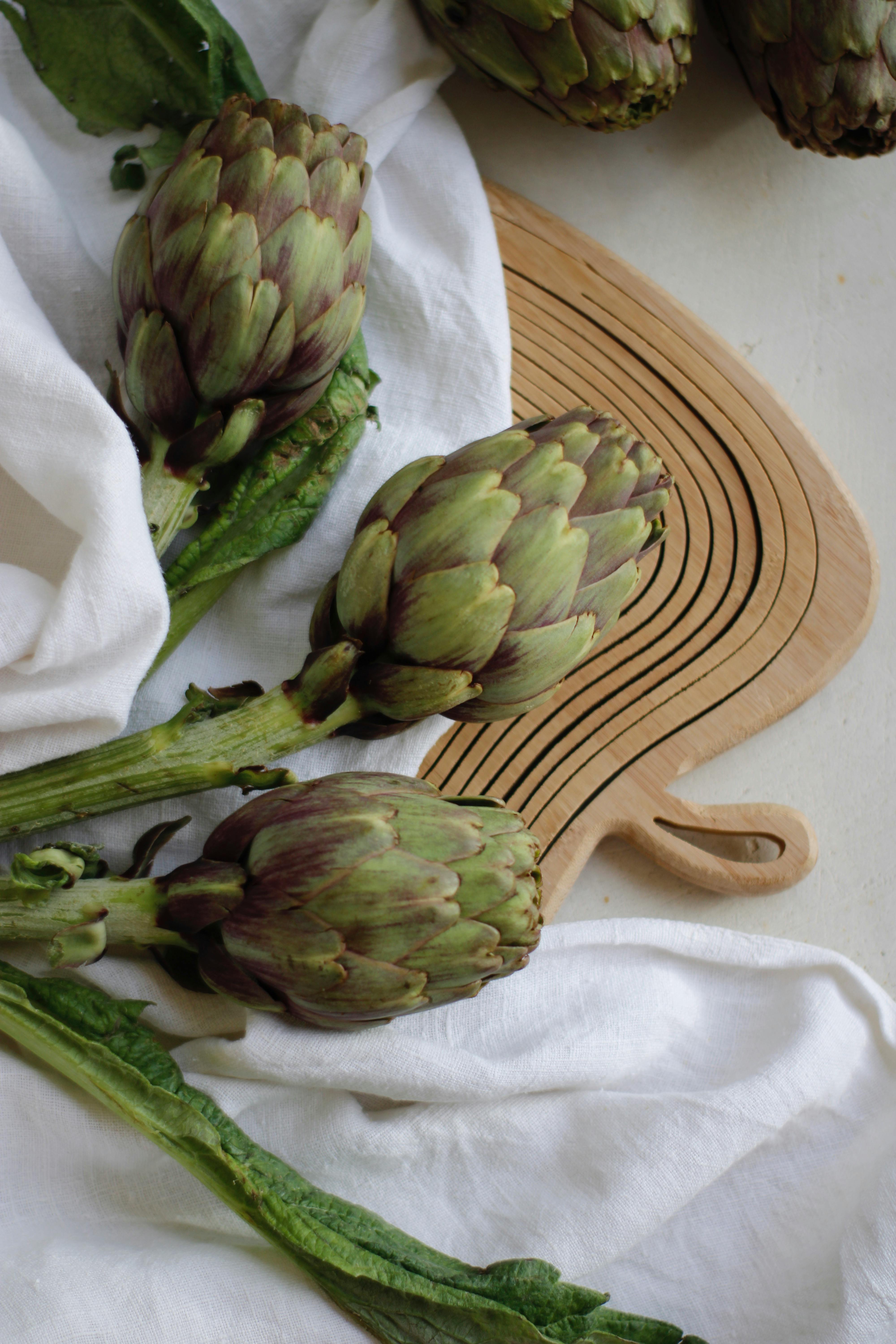 Three fresh artichokes on a wooden board with cloth, ideal for food blogs.