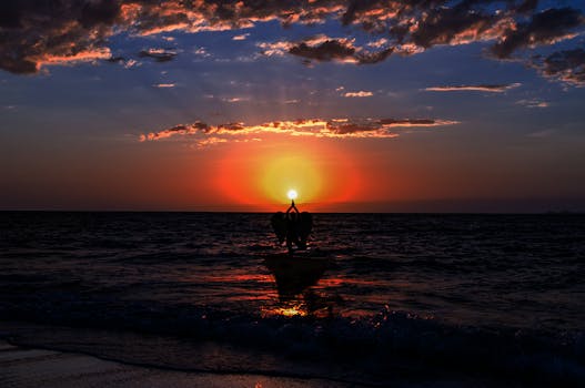 A tranquil scene of a person practicing yoga on a beach during a vibrant sunset, creating a reflective silhouette on the water.