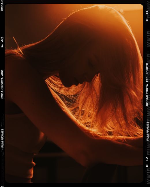 Artistic silhouette of woman with long hair in warm, dramatic lighting.