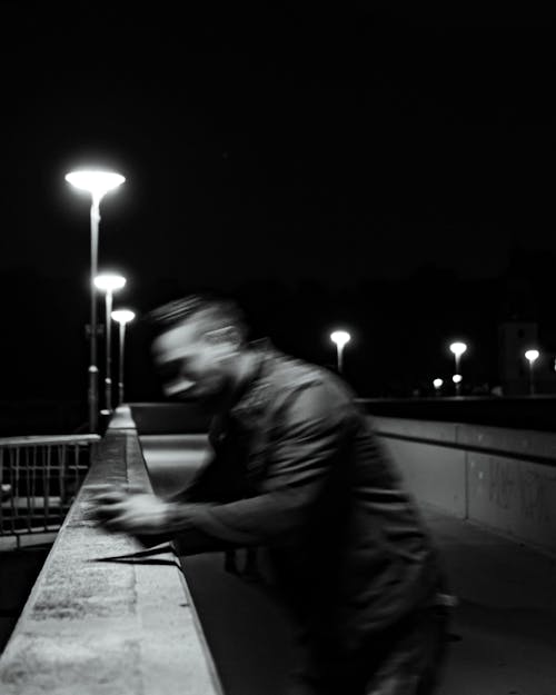 Grayscale Photo of a Man Standing on the Bridge