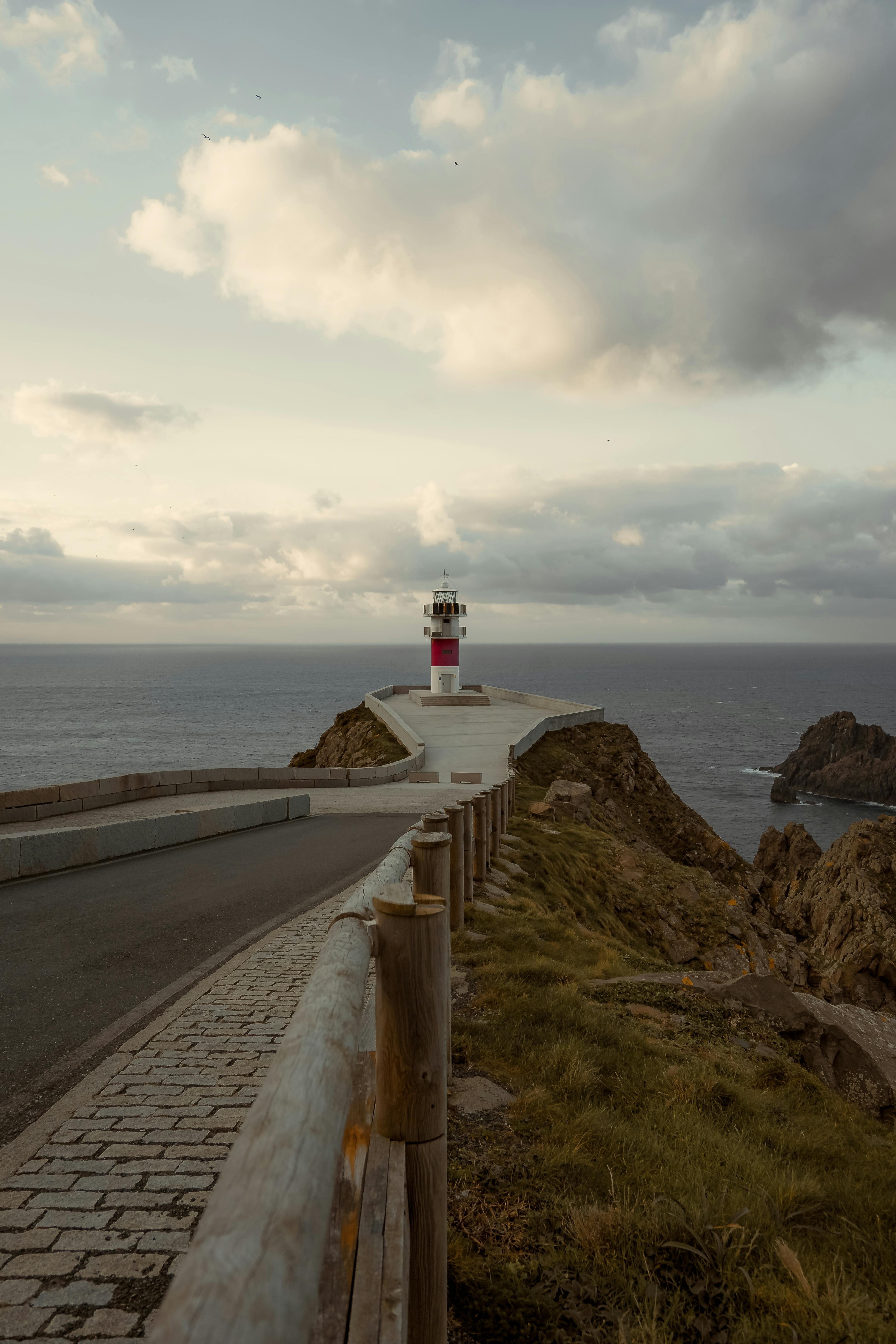 Explore the serene landscape of a lighthouse on a coastal road in Cariño, Spain under a cloudy sky.