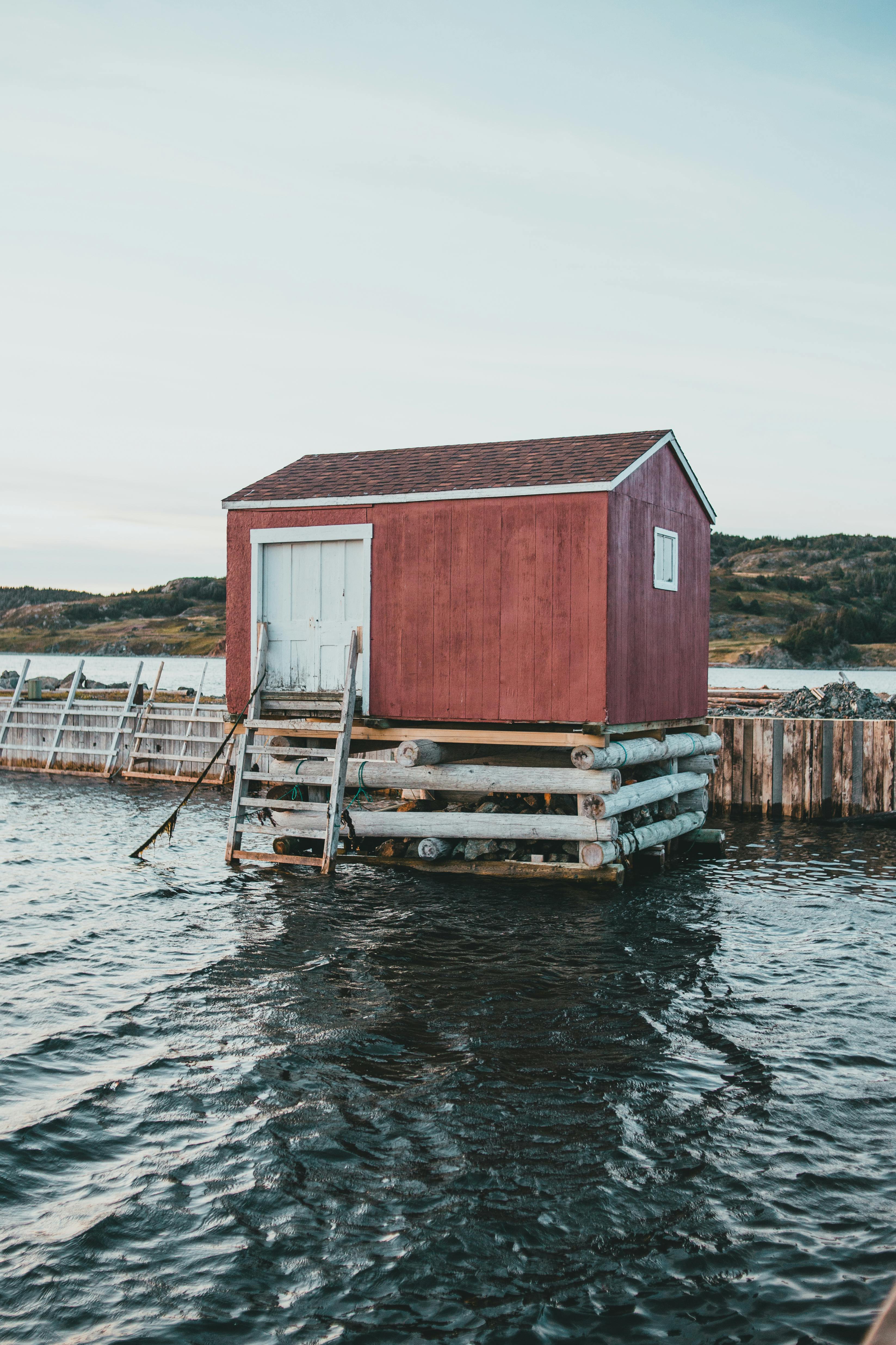 Charming red cabin on a wooden pier by the water, showcasing serene morning tranquility.