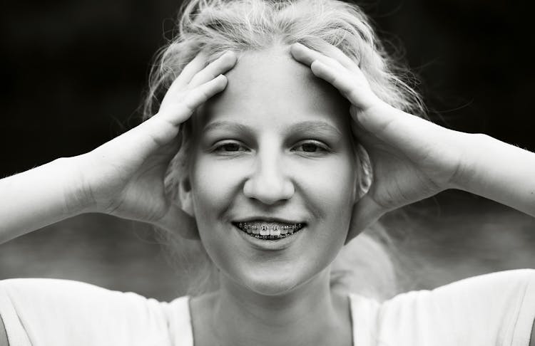 A Woman With Braces Smiling With Her Hands On Her Head