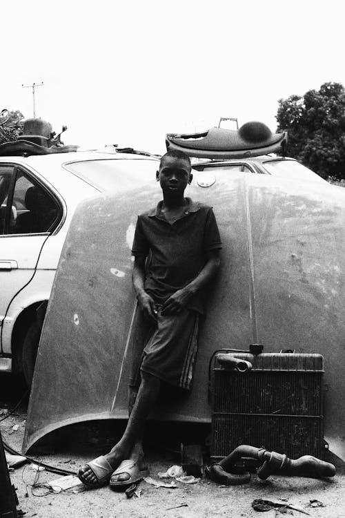 A Young Boy Standing while Leaning on a Car Hood