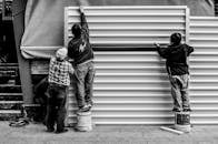 黑白照片显示，三名工人站在水桶上，在户外组装金属板