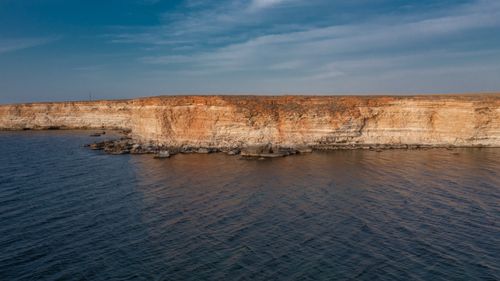 Free Stunning aerial view of rugged coastal cliffs meeting the ocean under a clear blue sky. Stock Photo