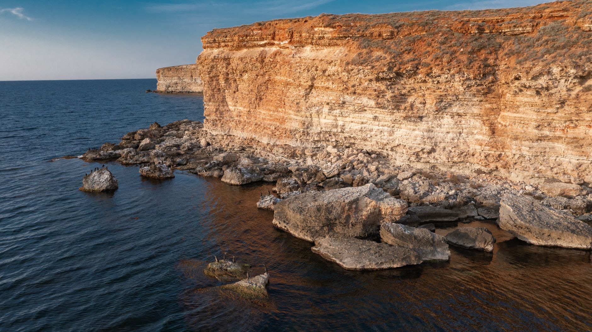 Camera operator filming on a coastal cliff path with the sea behind