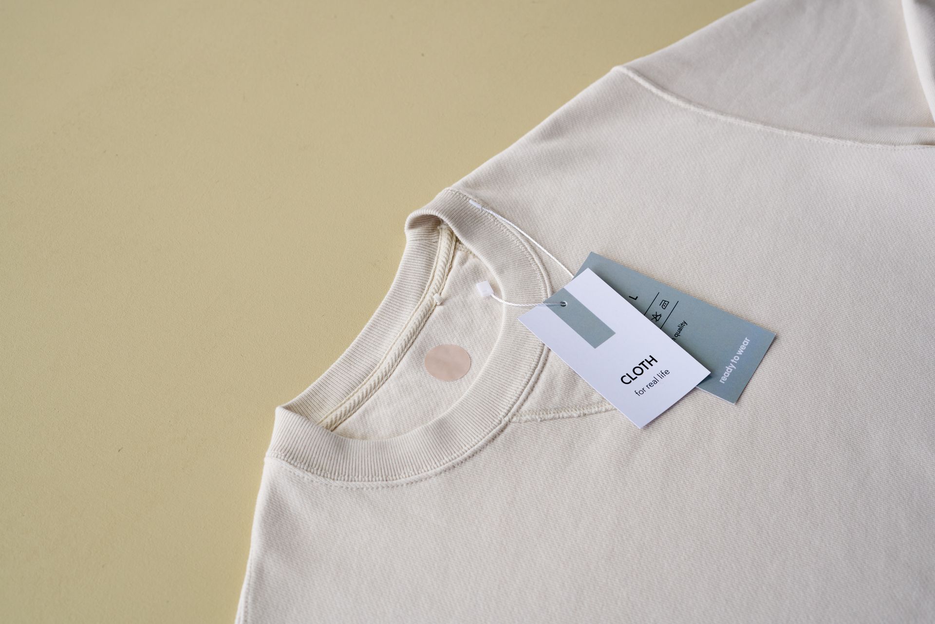 Minimalist beige sweatshirt with clothing tags on yellow background