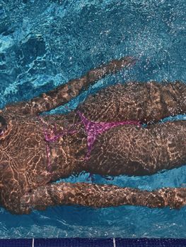 A woman in a bikini swims underwater in a clear blue pool, showcasing leisure and summer vibes.