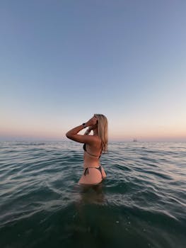 A woman in a swimsuit enjoys the ocean at sunset, creating a peaceful and relaxed mood.