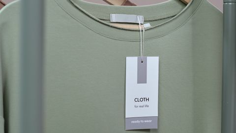 A simple green t-shirt with a tag hanging on a wooden hanger against a neutral background.