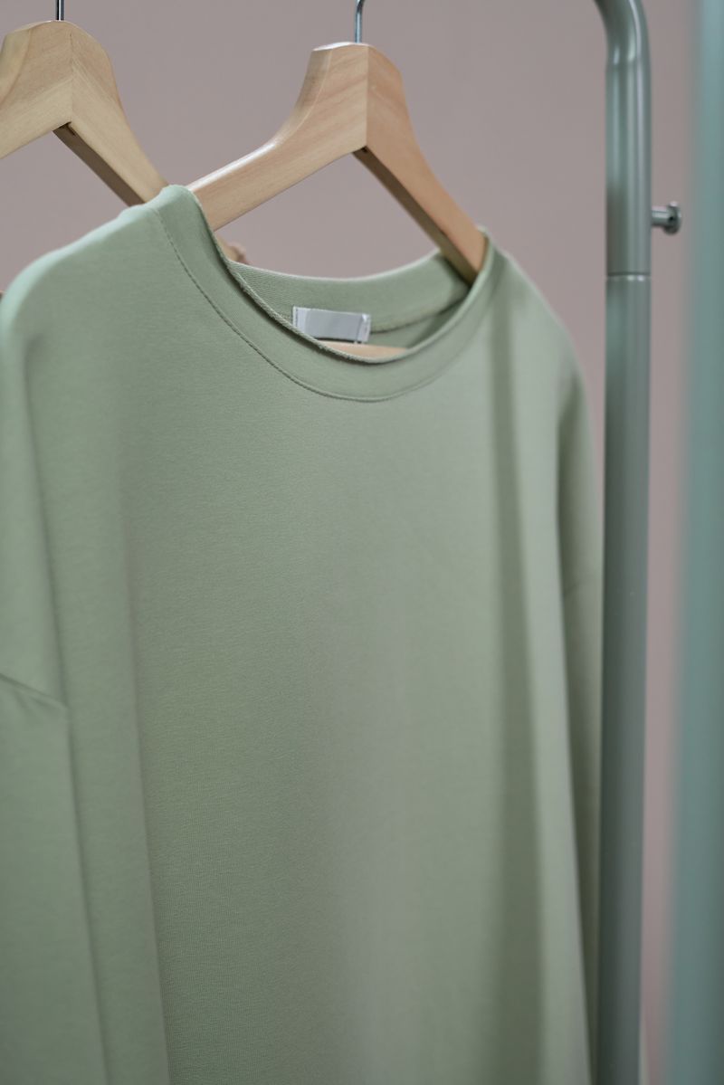 Sage green crewneck sweatshirt on a wooden hanger — photo by Ron Lach on Pexels