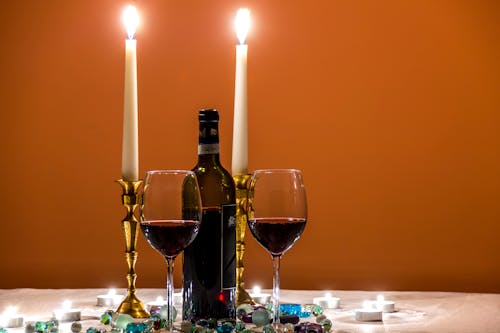 Два почти пустых бокала на длинной ножке рядом с бутылкой вина и зажженными свечами