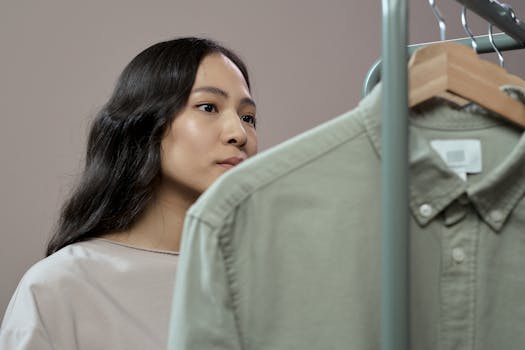 Asian woman thoughtfully browsing clothes in fashion studio, focusing on details.