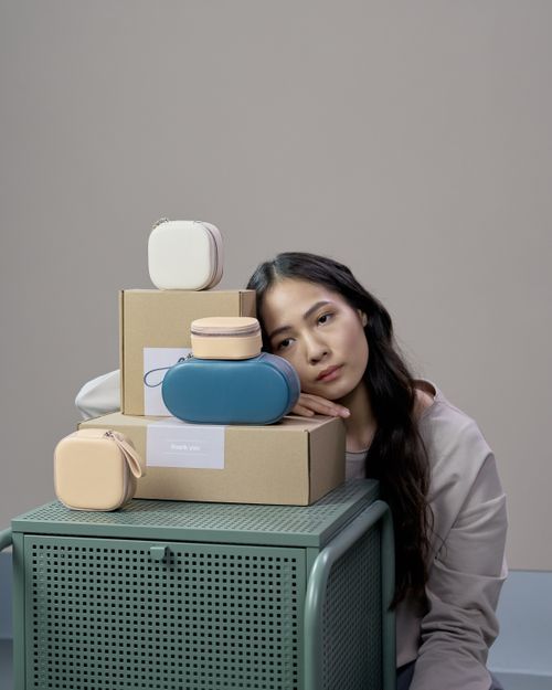 Free Studio portrait of a woman with small handbags and boxes against a grey background. Stock Photo