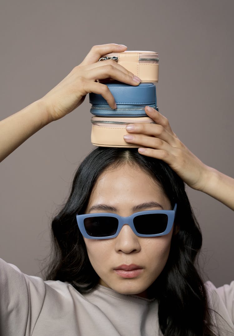 A Woman Wearing Sunglasses While Holding Pouches On Her Head