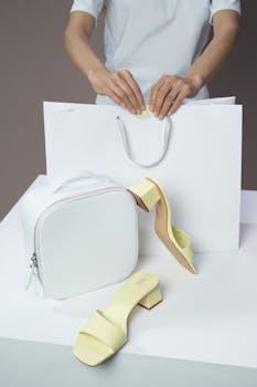 Elegant setup of white handbag and yellow sandals with a shopping bag.