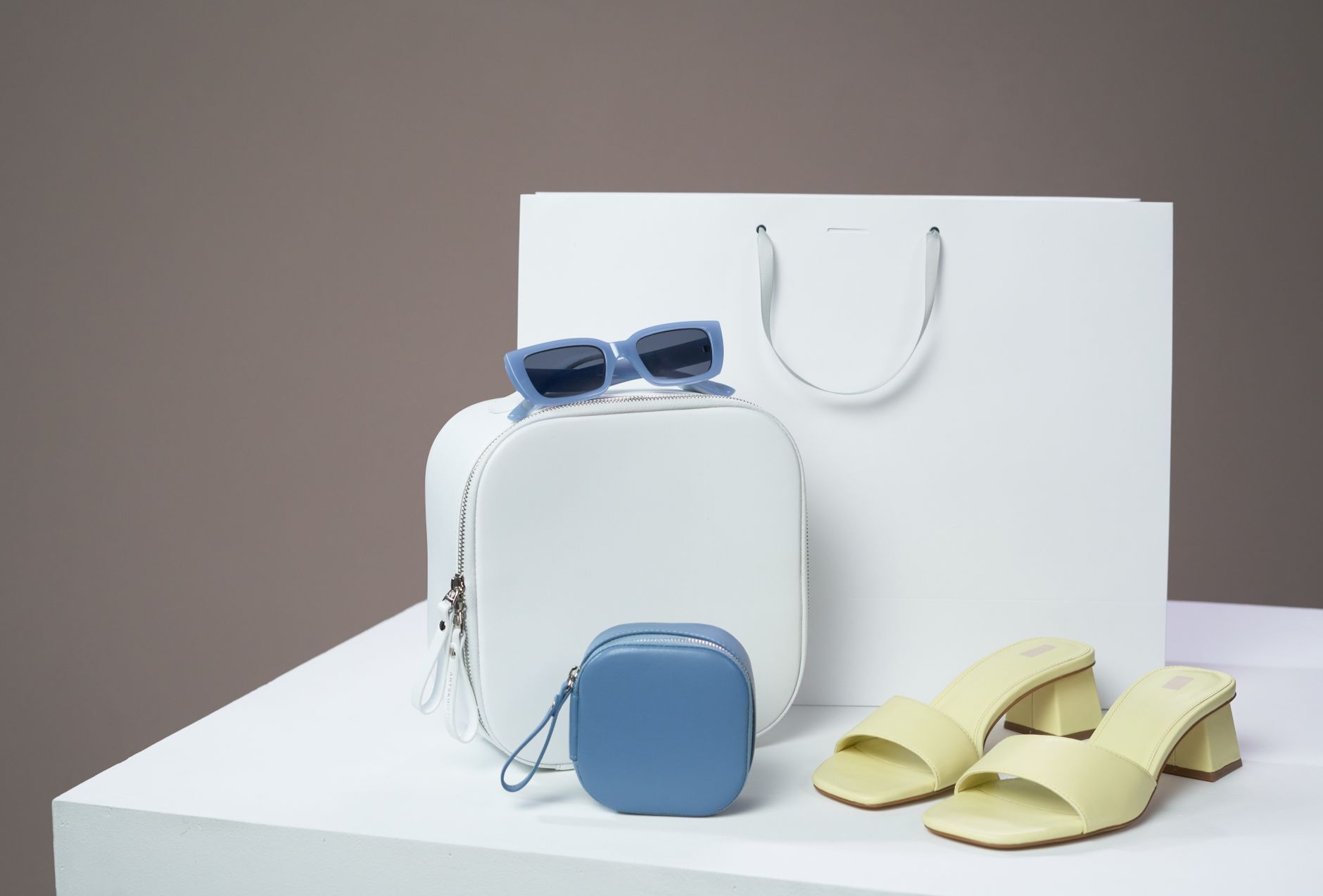 Modern women's fashion accessories including bags, sandals, and sunglasses on a minimalist platform.
