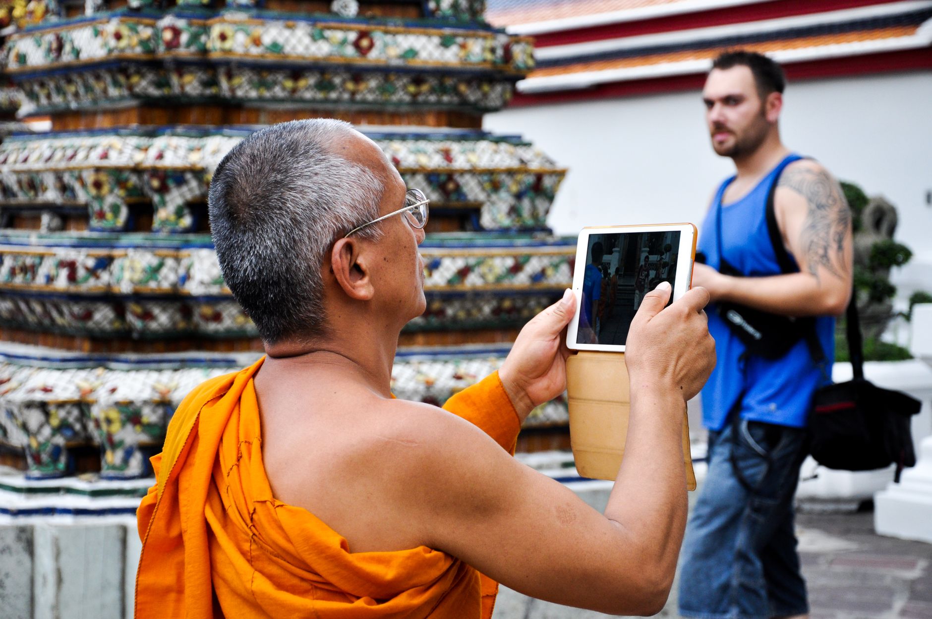 Monk using a tablet to photograph a temple in Thailand, capturing serene cultural moments.