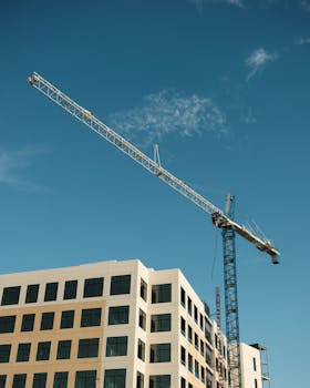 Tower crane at an urban construction site with a building and blue sky.