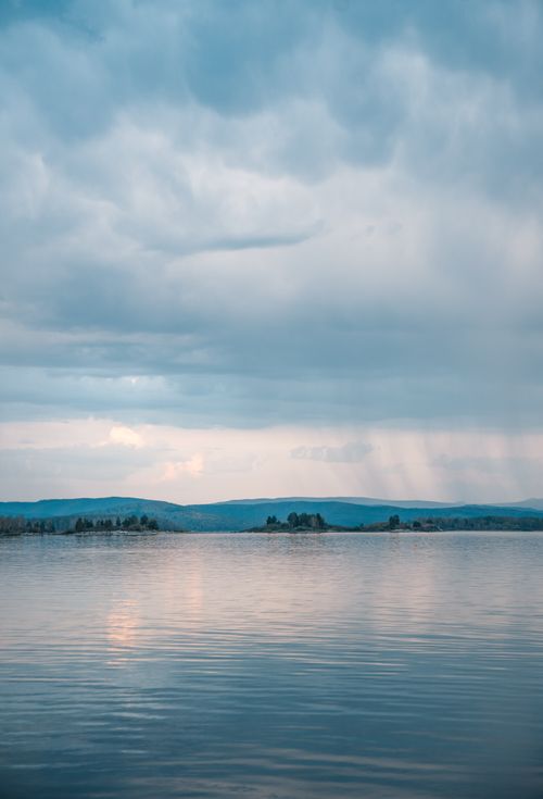 Free Calm lake reflecting the sky with moody clouds during sunset, offering a tranquil view. Stock Photo