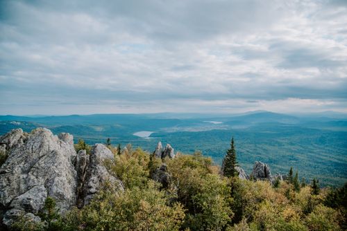 Free A breathtaking view of rocky mountain peaks and lush green forest under a cloudy sky. Stock Photo