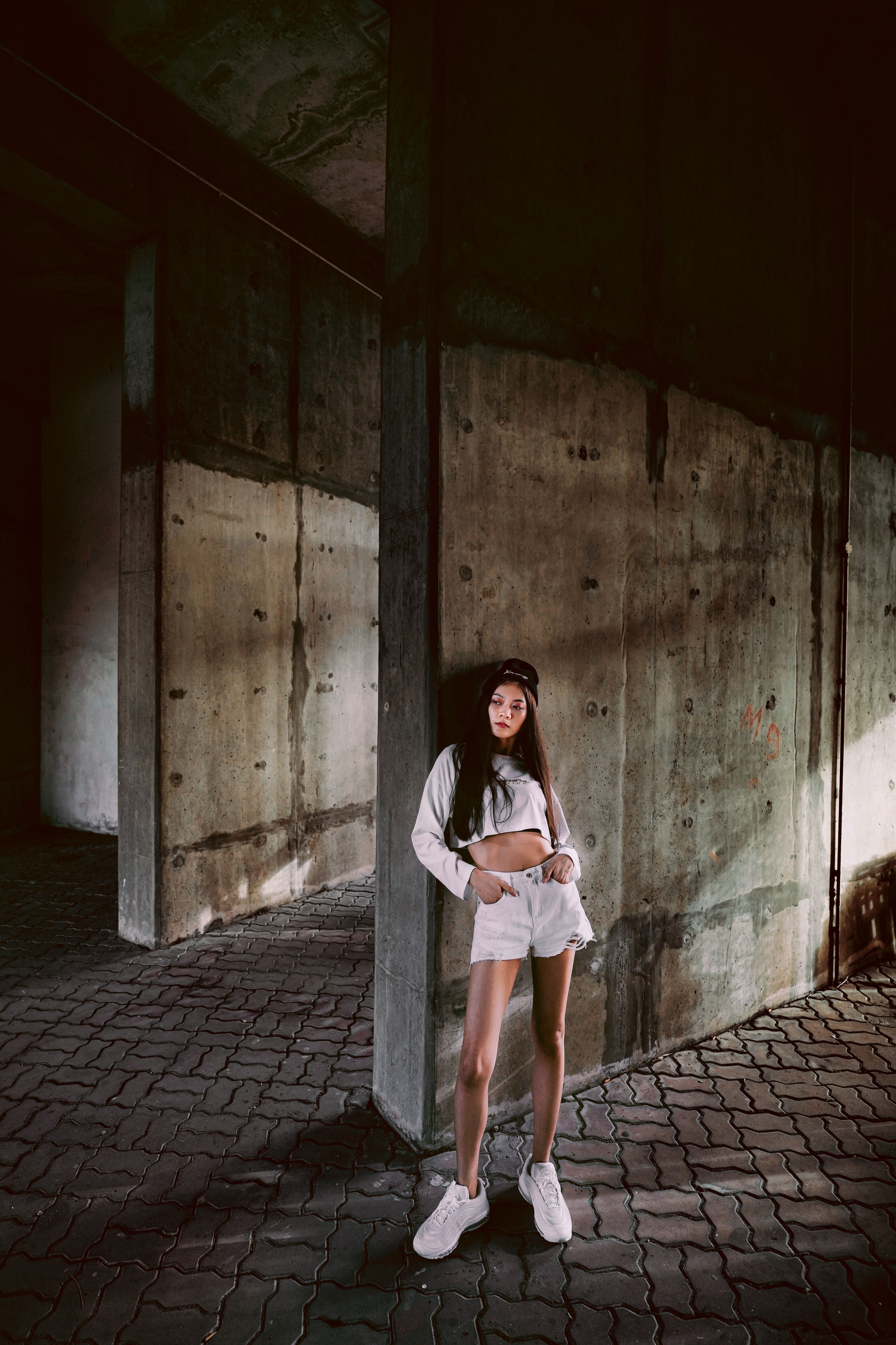 Stylish young woman in white outfit posing indoors against industrial background.