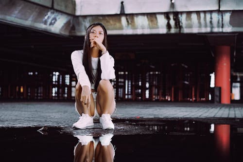 A Woman Crouching next to a Puddle of Water