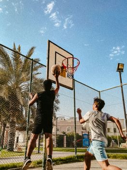 Two young men playing basketball together on an outdoor court under a clear blue sky.