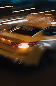 Dynamic shot of a yellow car with motion blur, captured at night, glowing with city lights.