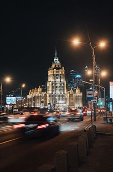 Illuminated city streets of Moscow with landmark building and bustling traffic at night.