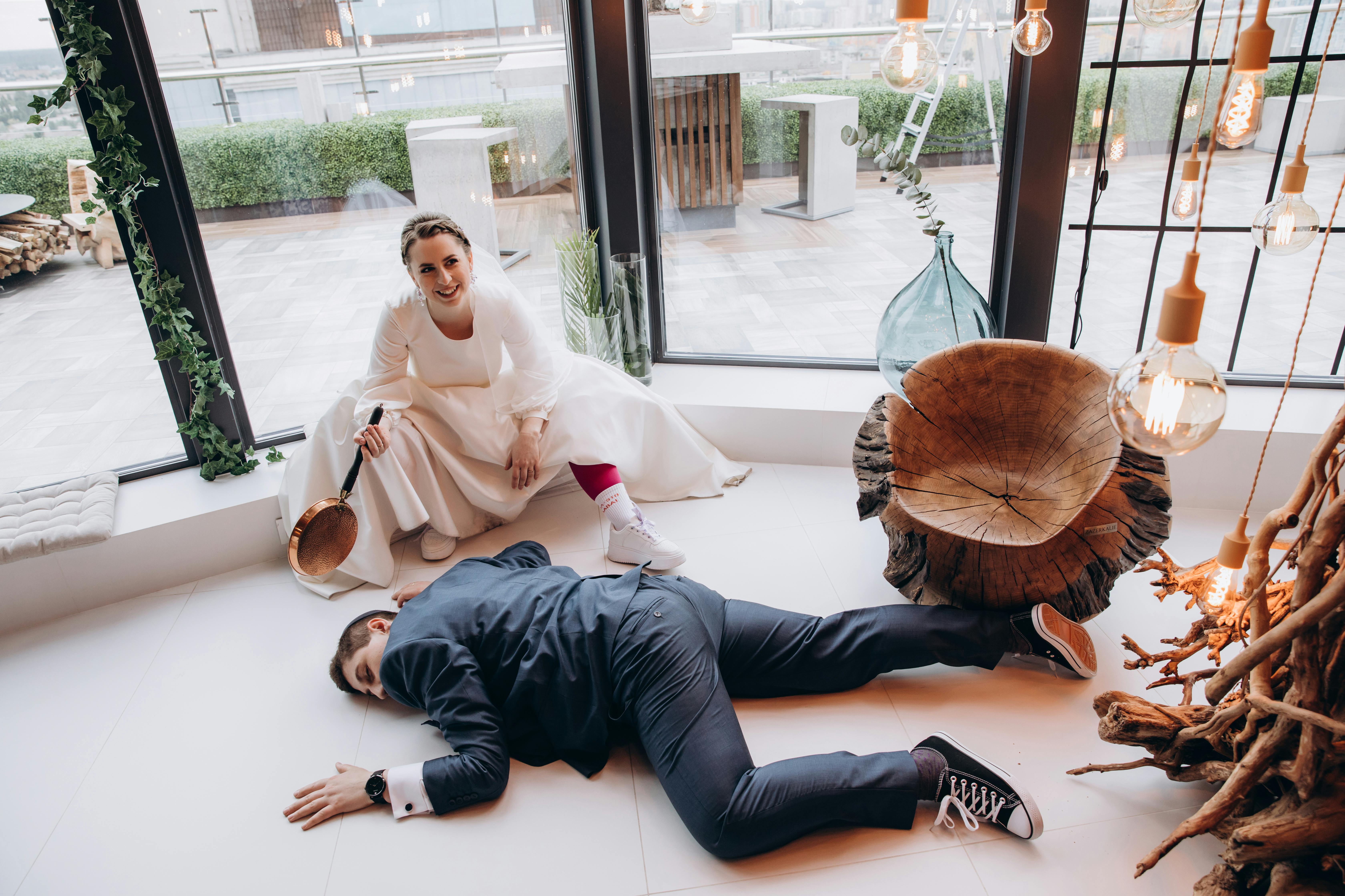 A playful wedding moment with a humorous bride holding a pan over an unconscious groom.
