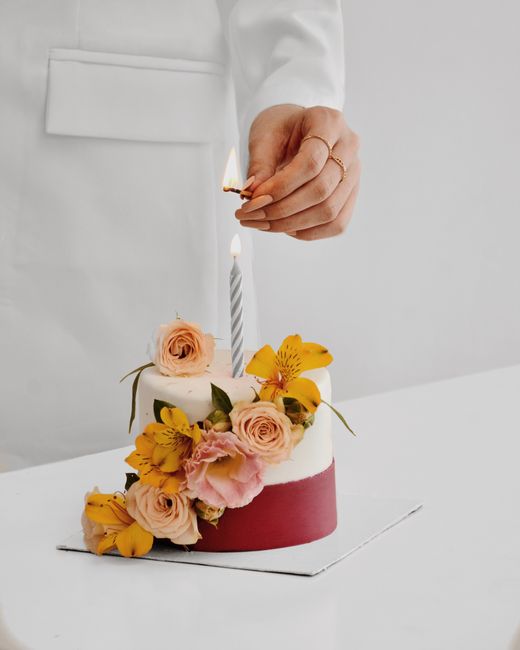 Stylish birthday cake adorned with pink and yellow flowers, candle lit by hand.