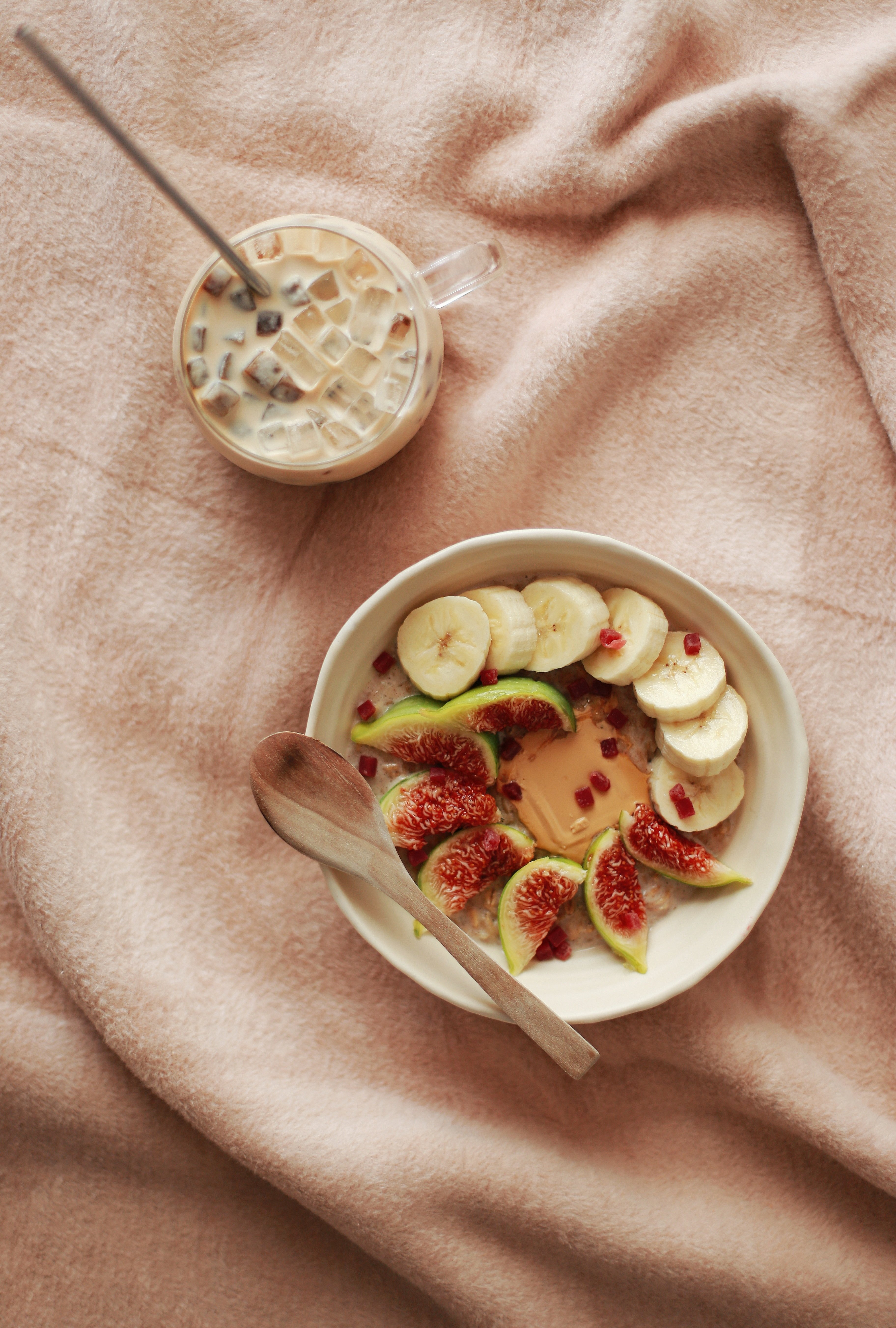 Top view of a fig and banana breakfast bowl with iced coffee on a soft blanket.