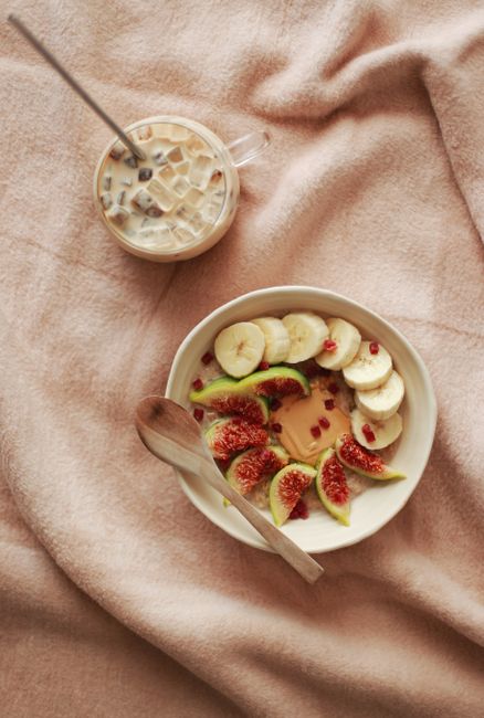 Top view of a fig and banana breakfast bowl with iced coffee on a soft blanket.