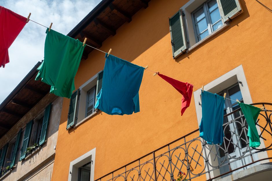 Vibrant clothes hanging on a line outside a rustic Italian building with colorful walls.