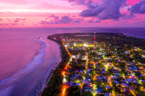 Free Stunning aerial view of a coastal city illuminated at dusk with vibrant skies and city lights. Stock Photo